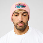 A man wearing a light pink knit beanie with a colorful embroidered graphic that reads 'FRESHLY BUCKED' in a graffiti-style font, paired with a white t-shirt against a light gray background.