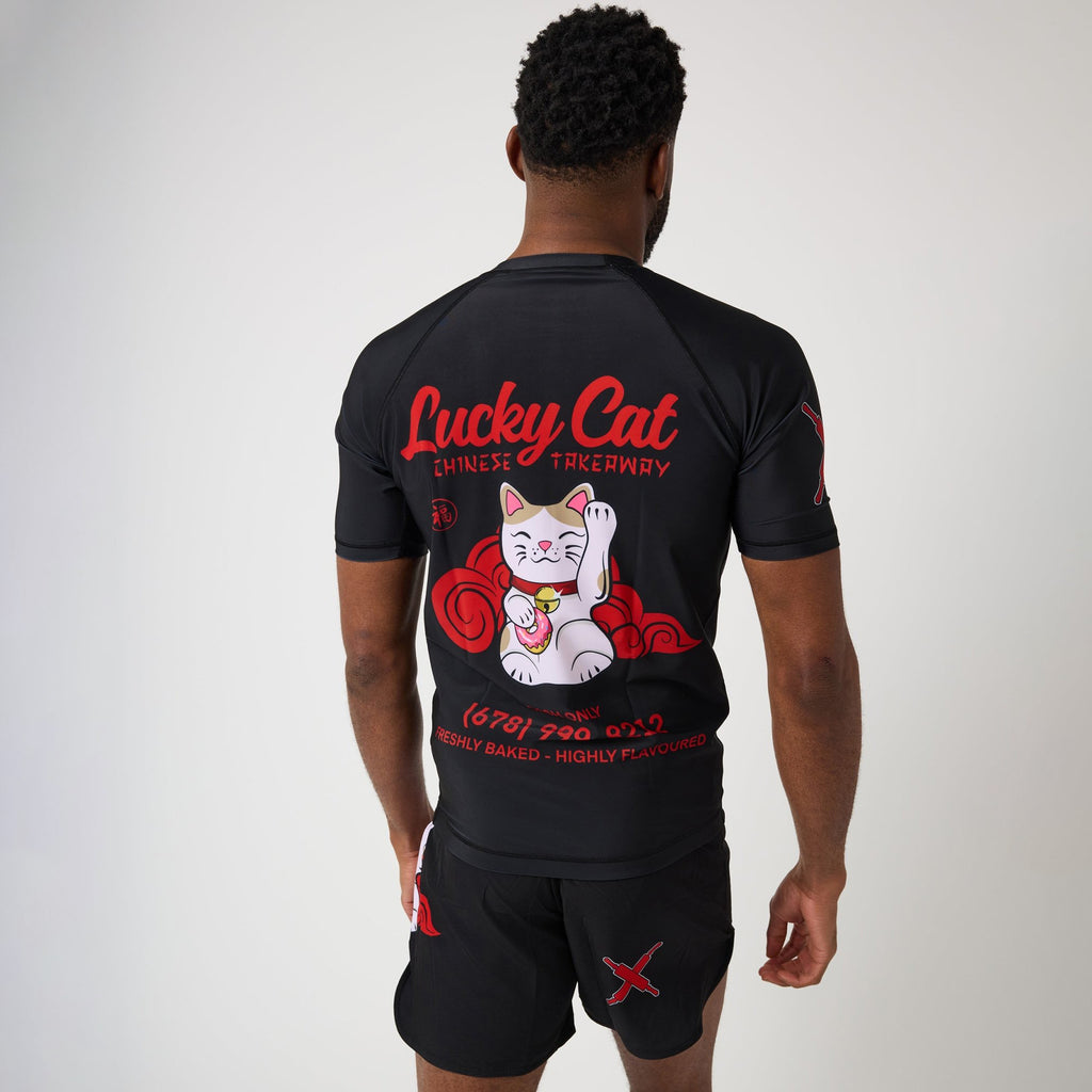 A man shown from the back wearing a black rash guard and matching shorts with a large red and white 'Lucky Cat' graphic on the back, photographed against a light gray studio background.