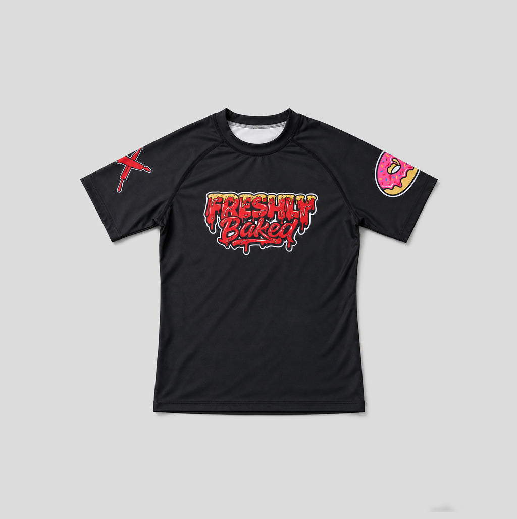 A black short-sleeve athletic t-shirt with a colorful 'Freshly Baked!' graphic on the chest, a red graphic on the right sleeve, and a pink donut graphic on the left sleeve, shown on a neutral gray background.