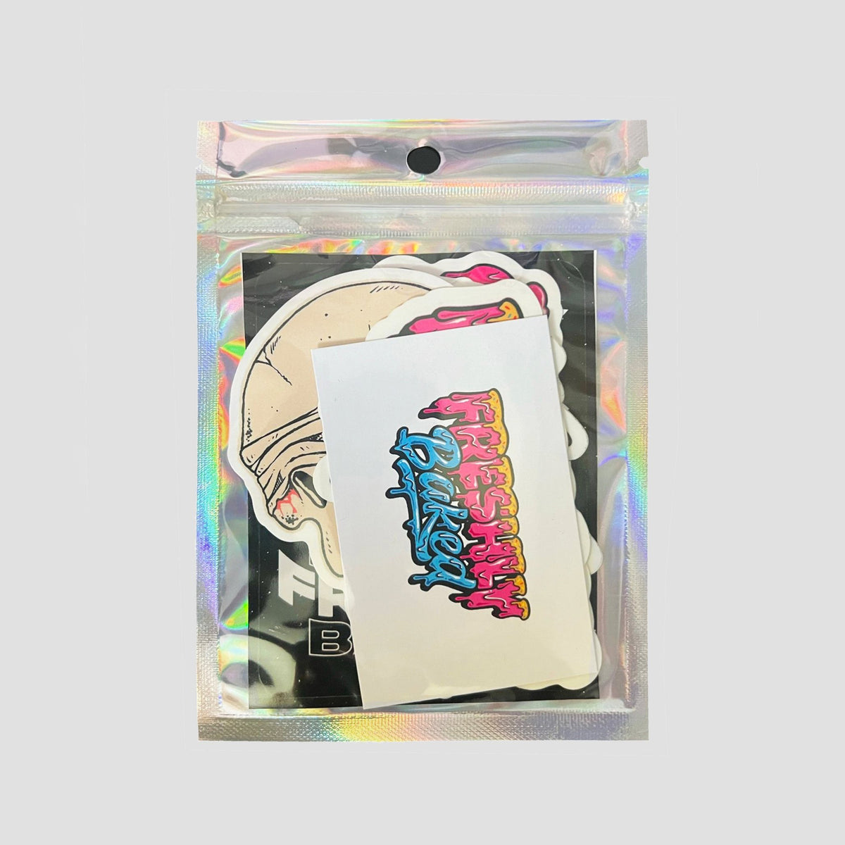 A clear holographic zip pouch containing a set of stickers, including a white die-cut sticker with colorful graffiti-style text reading 'Blessed' and an illustrated sticker of a person wearing a helmet, shown on a light gray background.